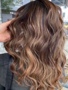 Caramel-hellbraune Foliage-Haarfarbe für eine wellige Langhaarfrisur, gestylt vom Friseur HappyHairHarburg in Hamburg.