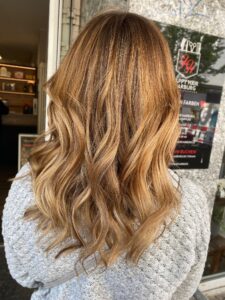 Gold-braune Haarfarbe mit Babylights für eine wellige Langhaarfrisur, gestylt vom Friseur HappyHairHarburg in Hamburg.