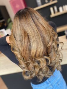 Caramel-hellbraune Haarfarbe mit Foliage-Technik für eine wellige Langhaarfrisur, kreiert vom Friseur HappyHairHarburg in Hamburg.