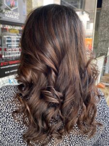 Schokolade-braune Balayage-Haarfarbe für eine wellige Langhaarfrisur, gestylt vom Friseur HappyHairHarburg in Hamburg.