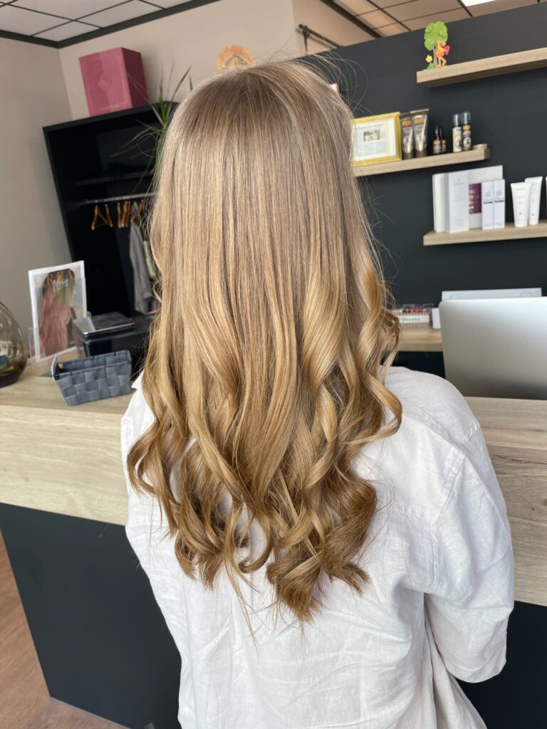 Warme, hellbraune Foliage-Strähnchen auf welligem, langem Haar mit Redken-Produkten.